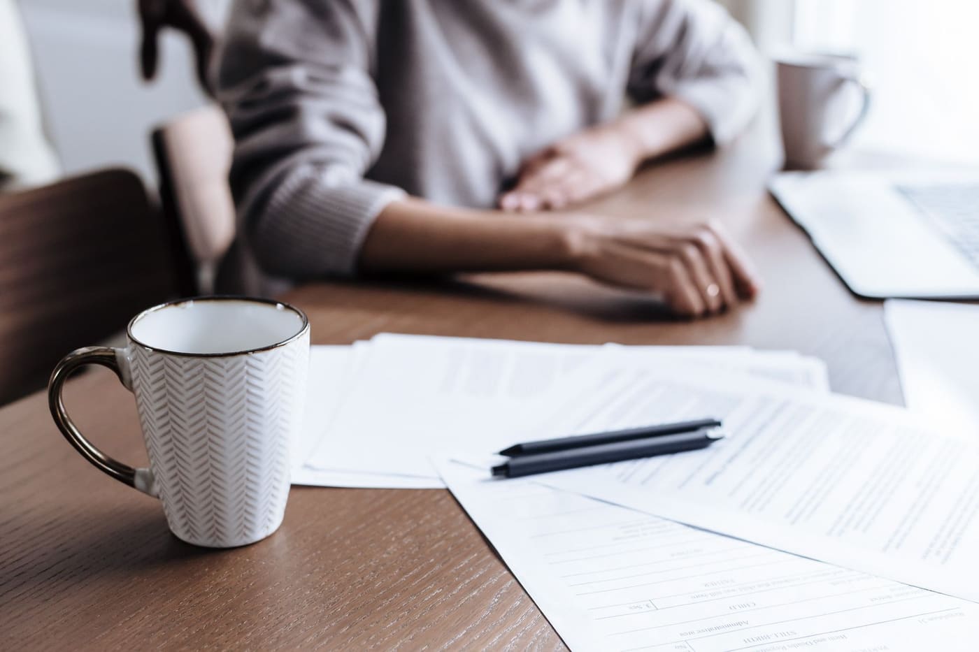 Papers, two pens and a white coffee mug on a wooden table