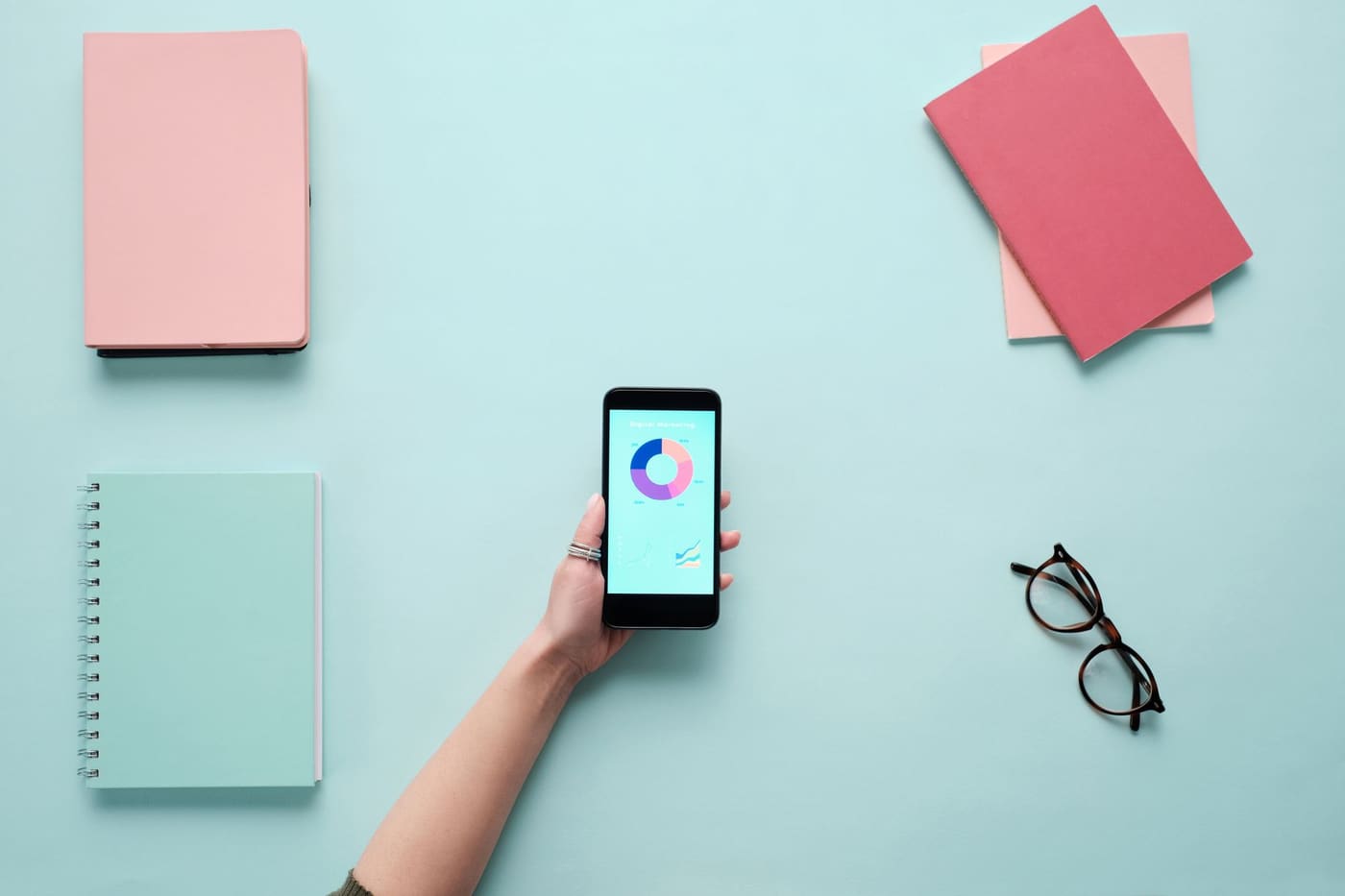 A smartphone showing a chart, with notebooks and glasses laid out around it