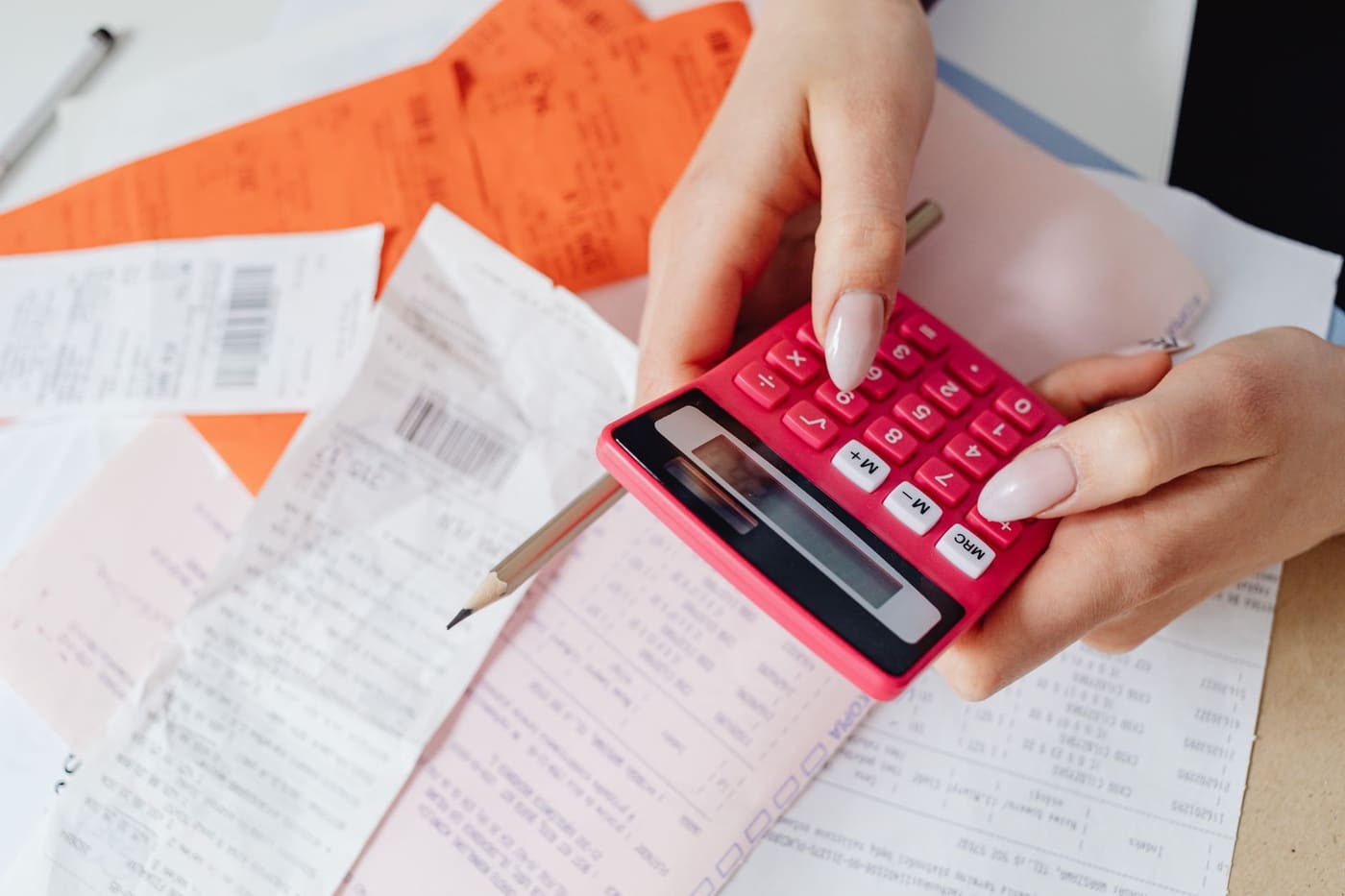 Hands holding a pink calculator over a desk covered in receipts