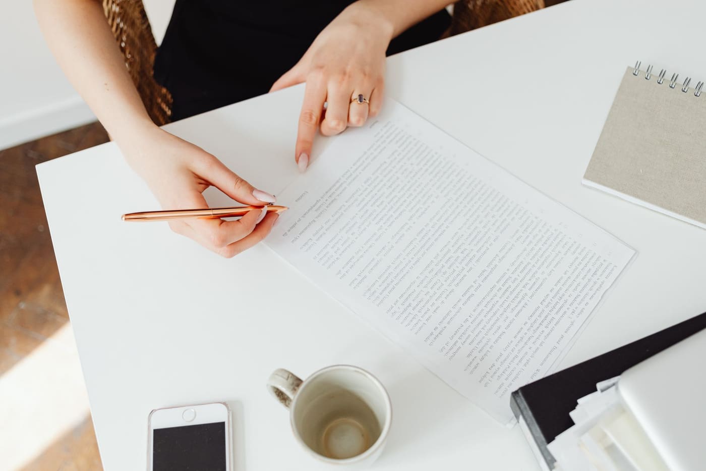 A person reviewing a printed document with a pen on a white desk