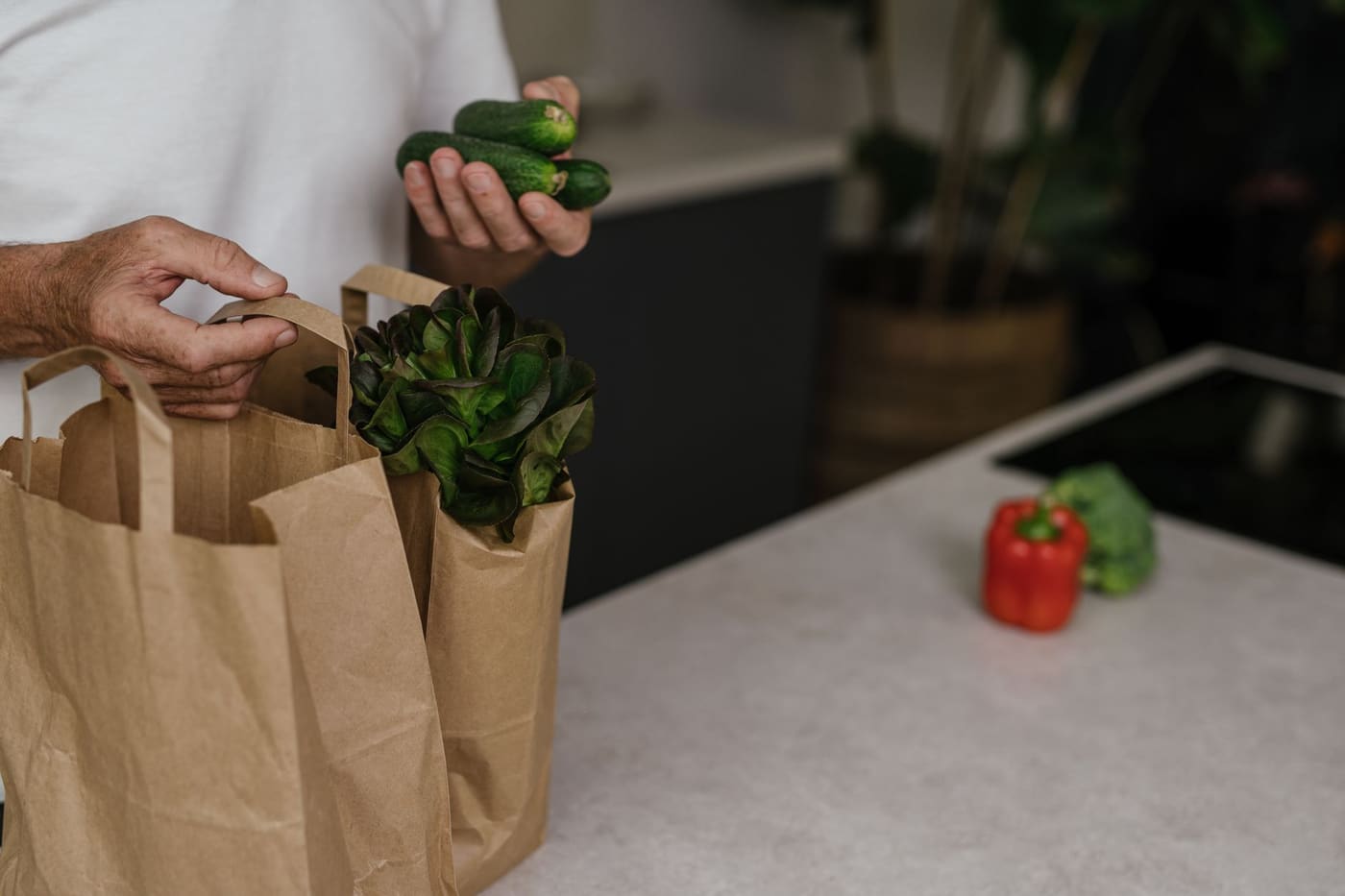 A person placing fresh vegetables into paper bags on a kitchen counter