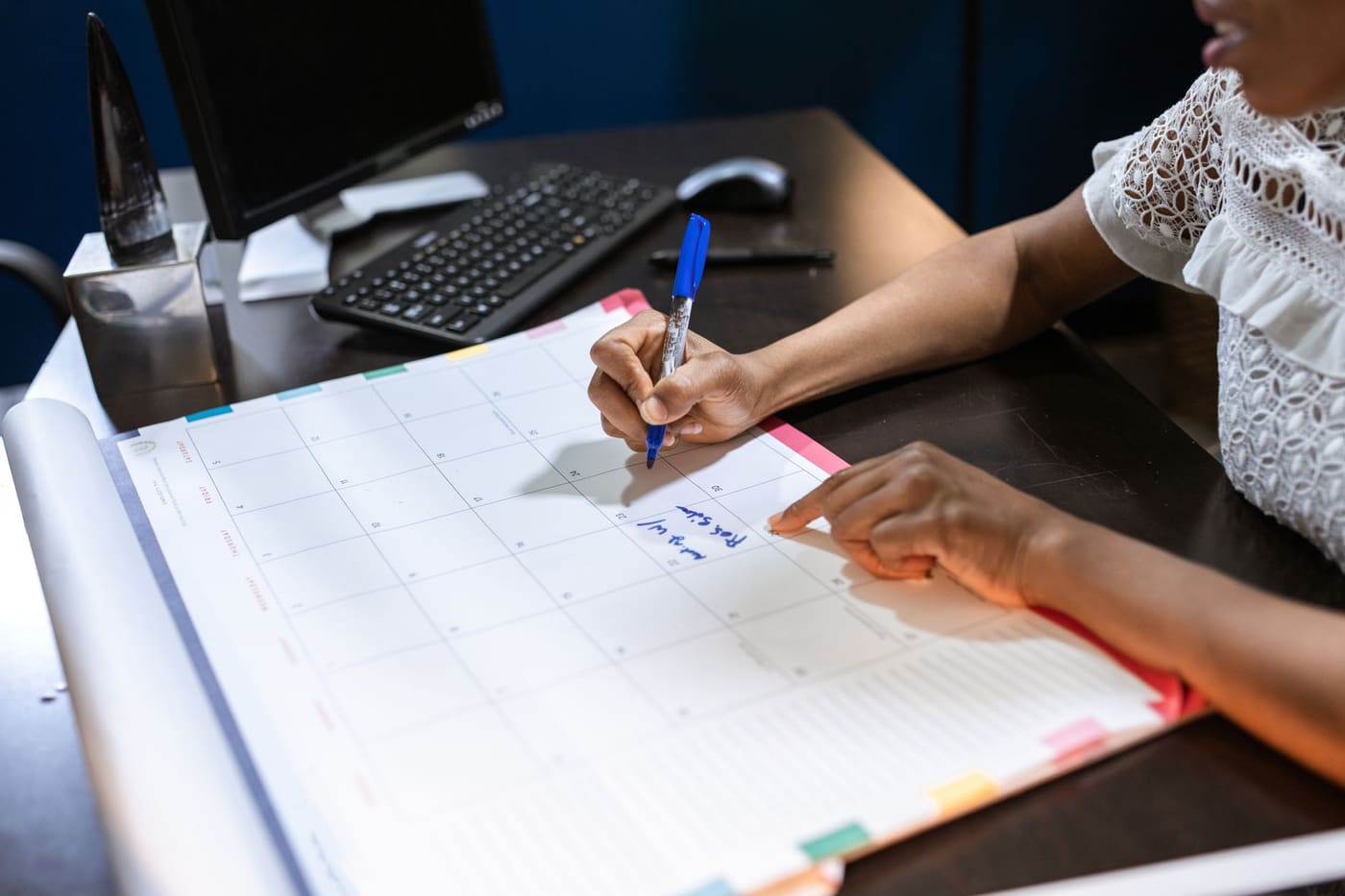 A person writing dates in blue marker on a large desk calendar